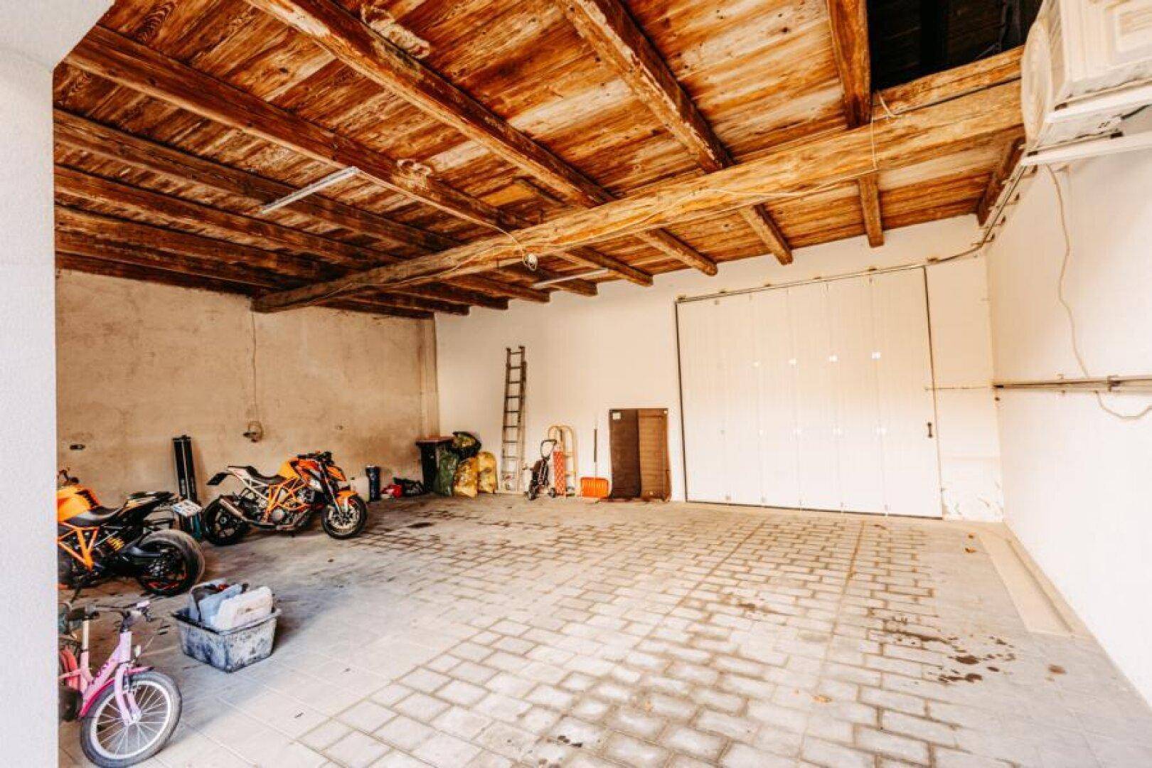 Geräumige Garage mit Ziegelpflasterboden, freiliegenden Holzbalken und Platz für Fahrzeuge.