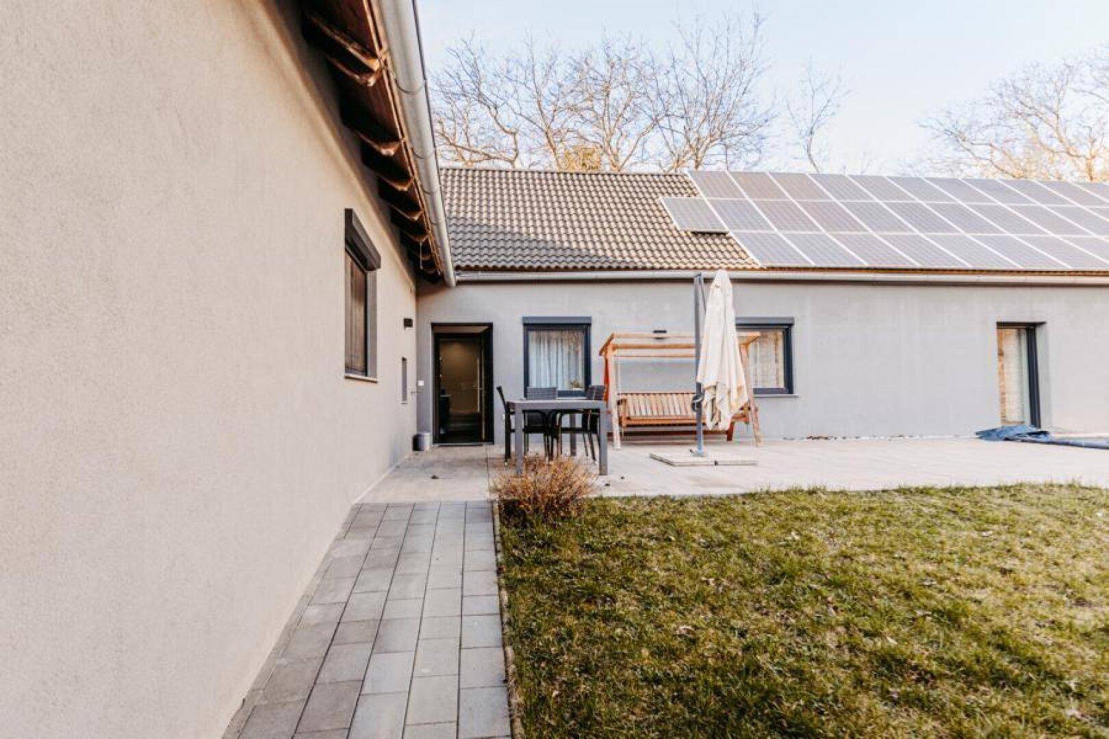Seitliche Ansicht des Hauses mit Zugang zur gefliesten Terrasse und Gartenbereich.