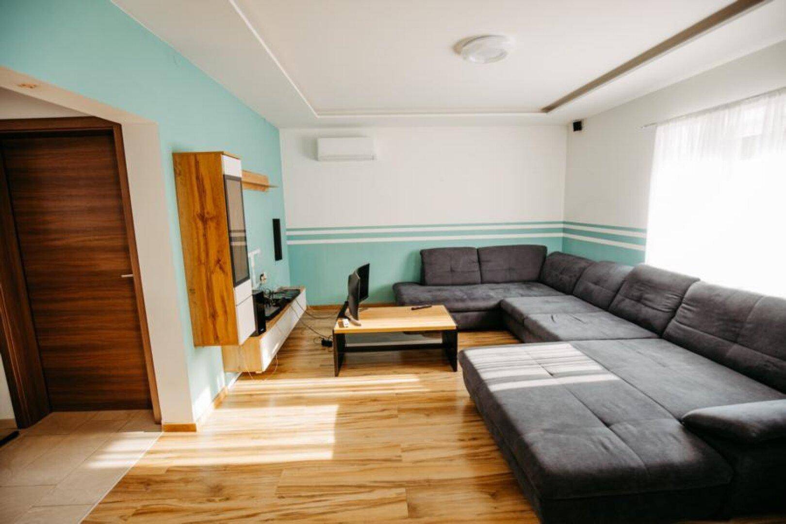 Helles Wohnzimmer mit großem Ecksofa, Holzboden und moderner Wandgestaltung in Türkis.