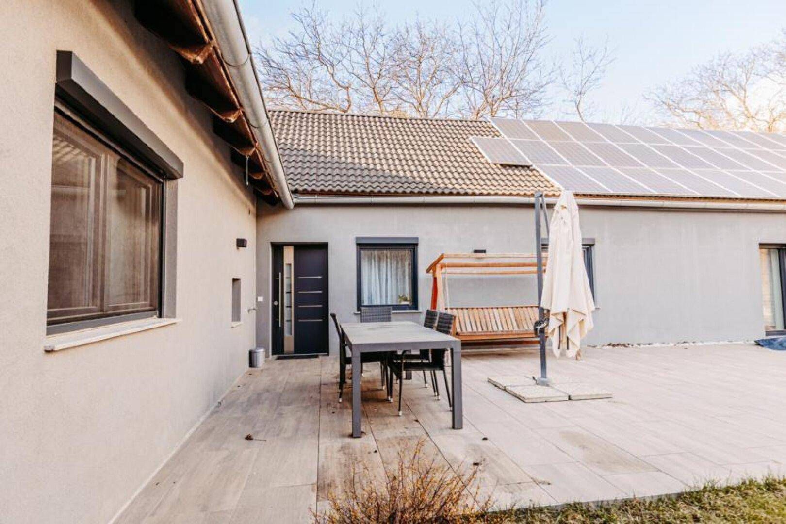 Terrasse mit Gartenmöbeln und Sonnenschirm, angrenzend an das Haus mit Solaranlage.