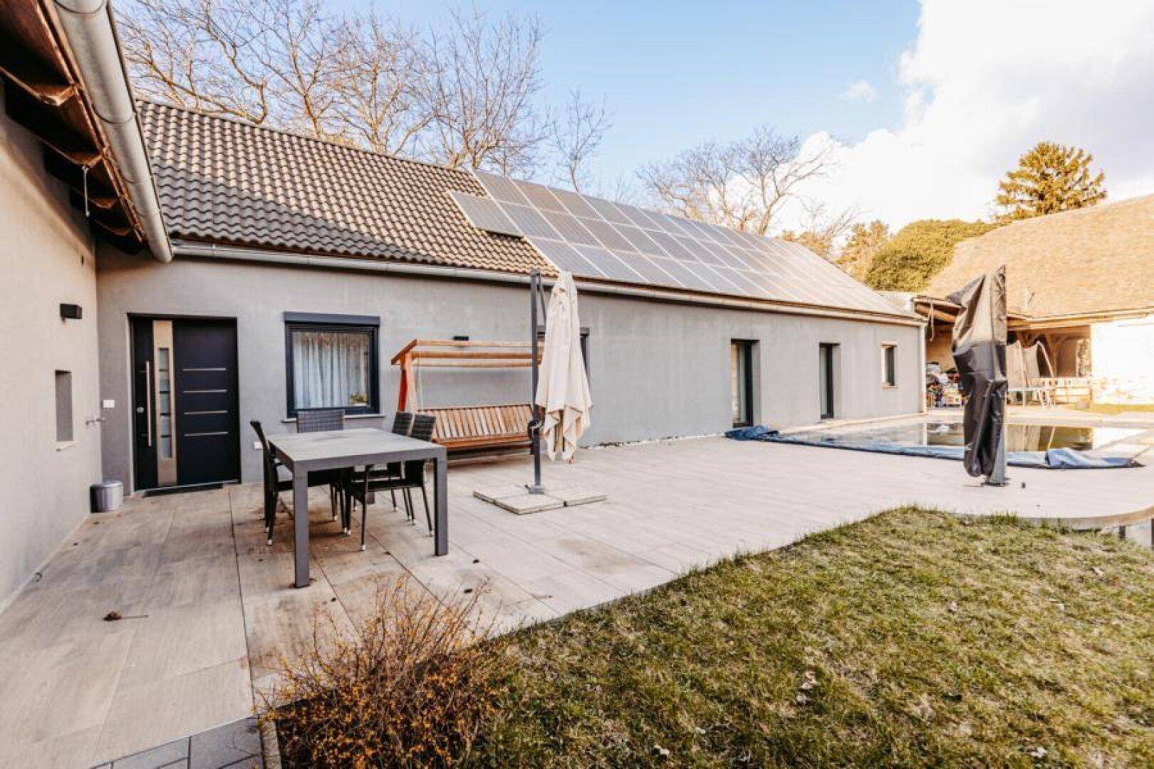 Weitläufige Terrasse mit Pool, Gartenmöbeln und Blick auf die Solaranlage auf dem Dach.
