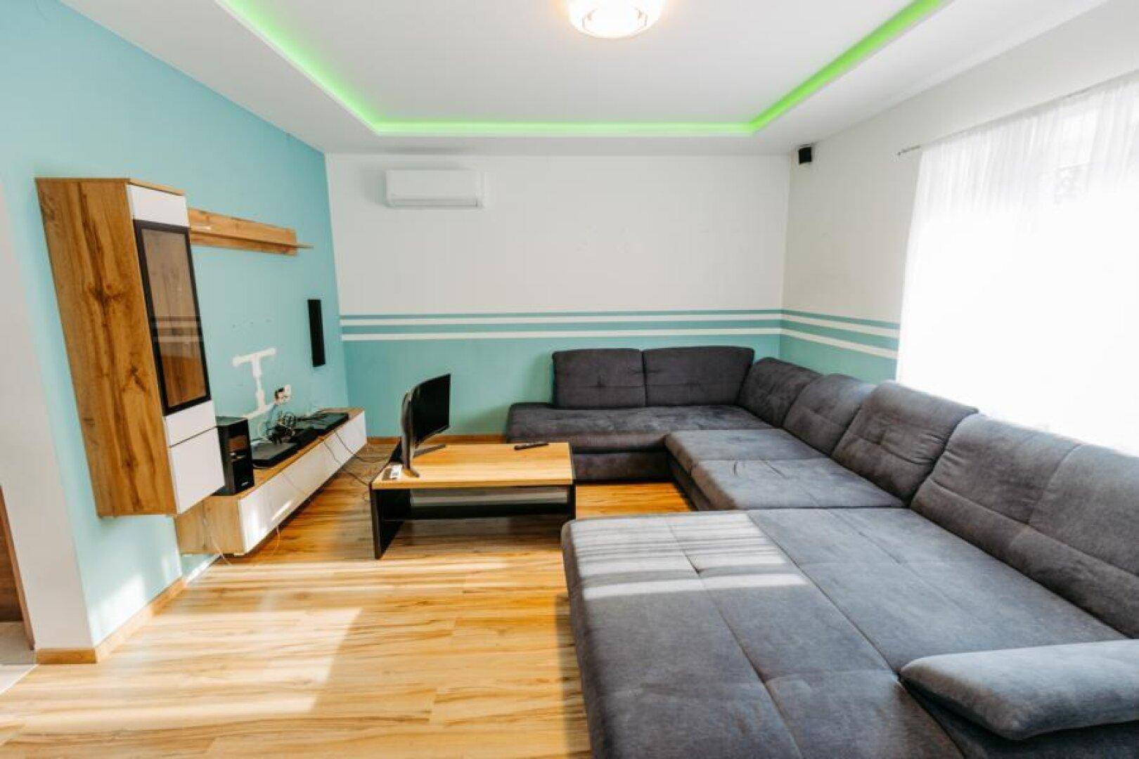 Modern eingerichtetes Wohnzimmer mit Ecksofa, Holzboden und Wanddekoration in Türkis und Weiß.