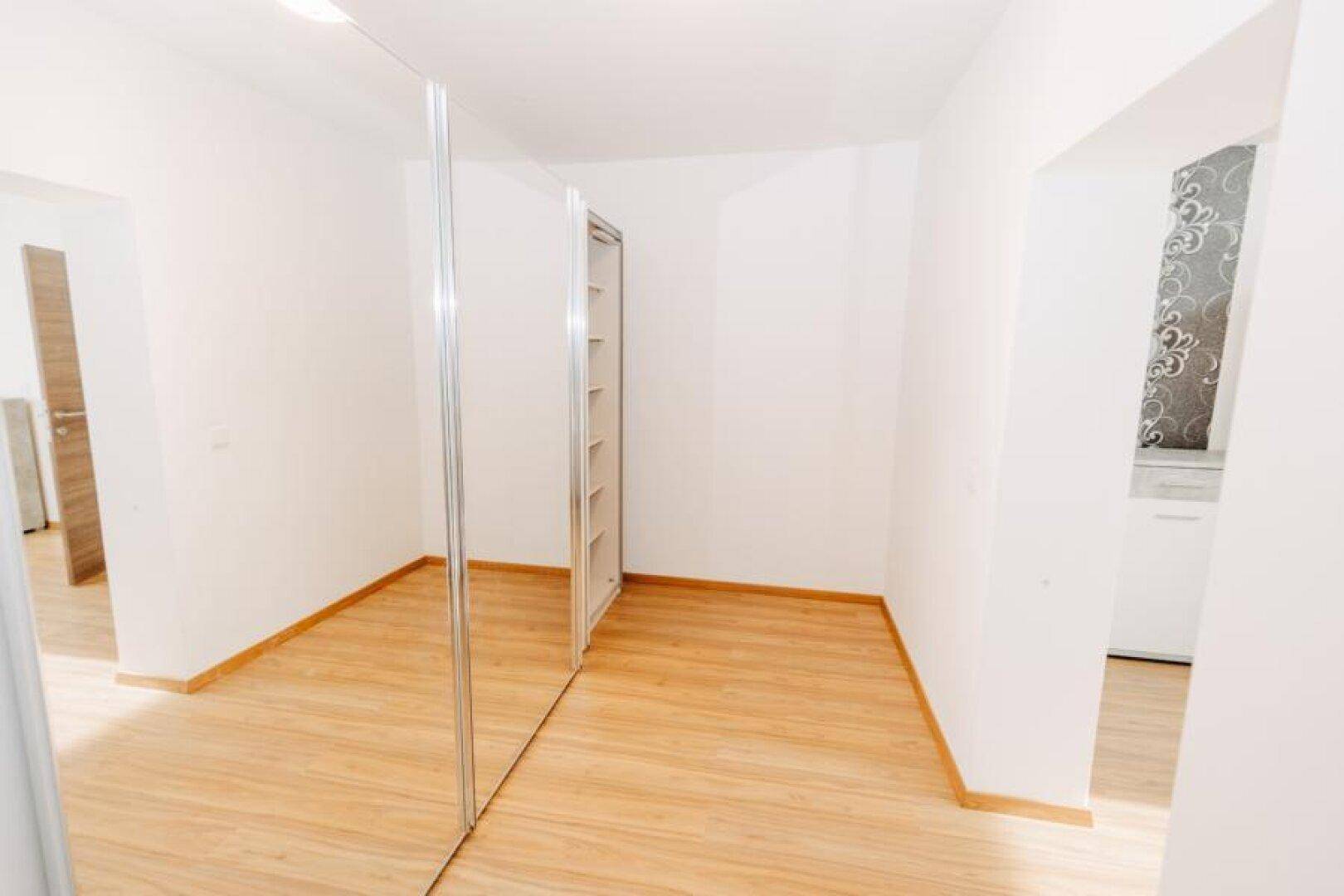 Leeres Zimmer mit Spiegelschränken und hellem Holzboden, ideal als Ankleidezimmer.