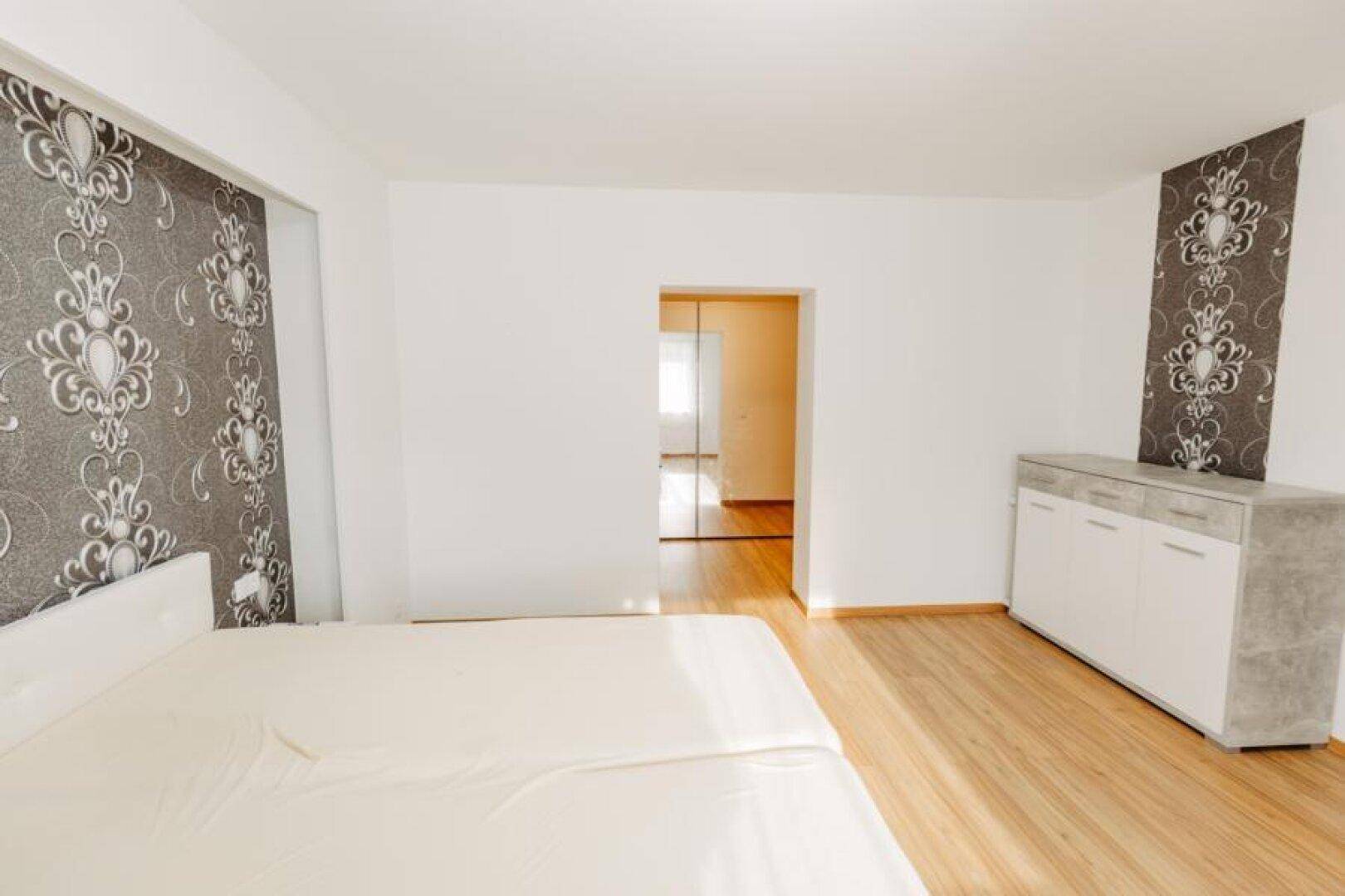 Schlafzimmer mit Doppelbett, Holzboden und stilvoller Tapete, die einen Akzent setzt.