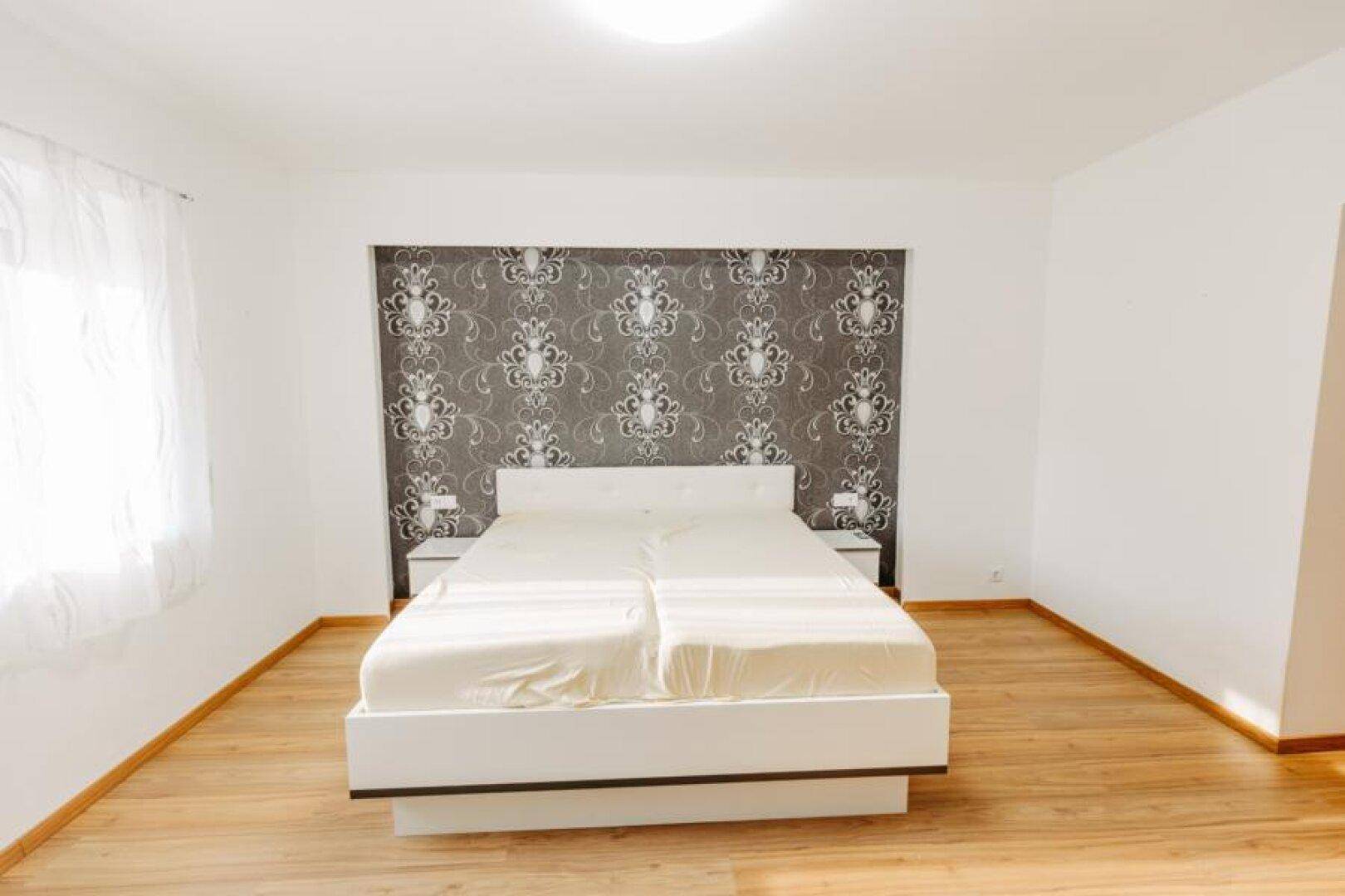 Helles Schlafzimmer mit Doppelbett, Holzboden und dekorativer Tapete an der Wand.