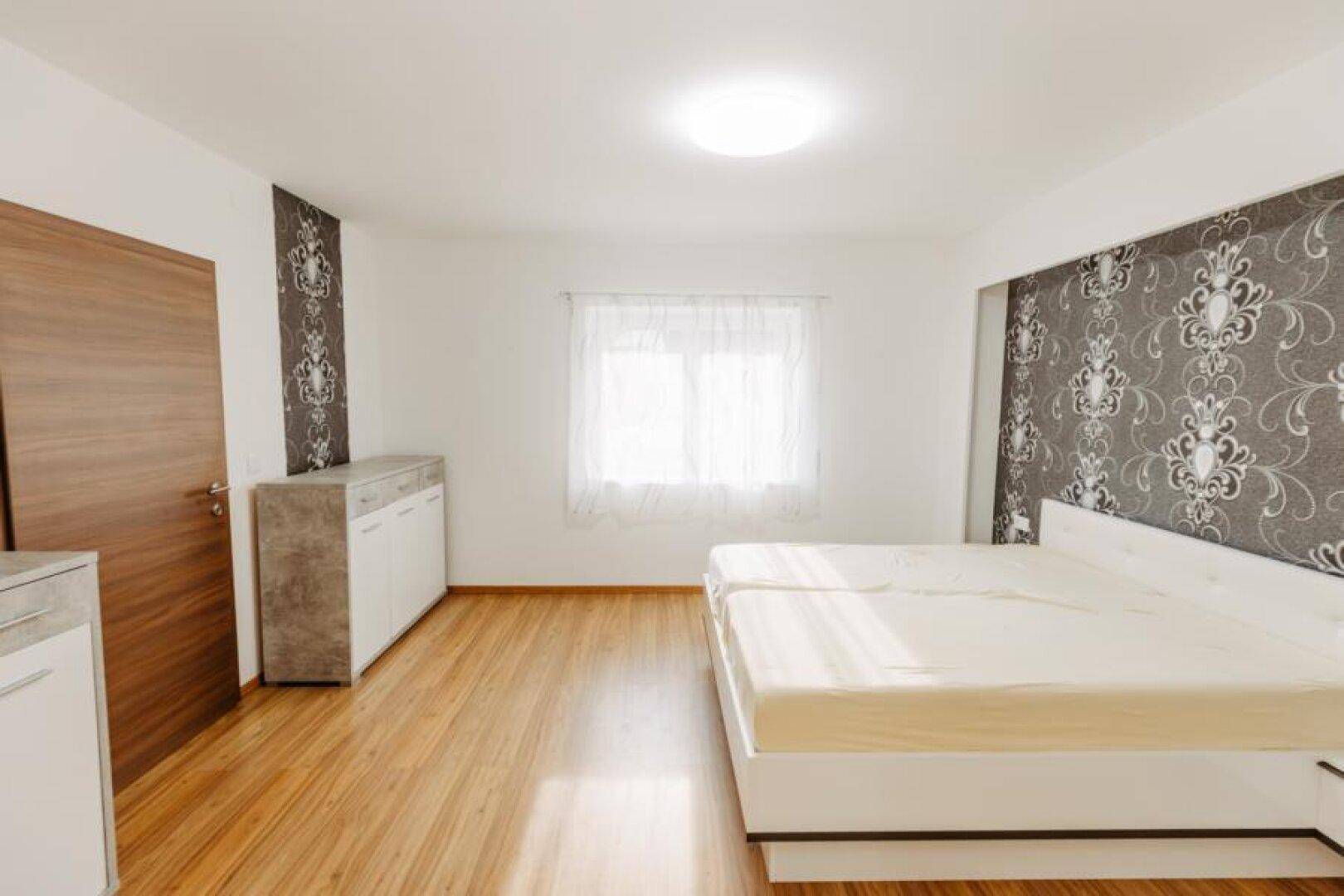 Gemütliches Schlafzimmer mit Holzboden, Doppelbett und Fenster für viel Tageslicht.