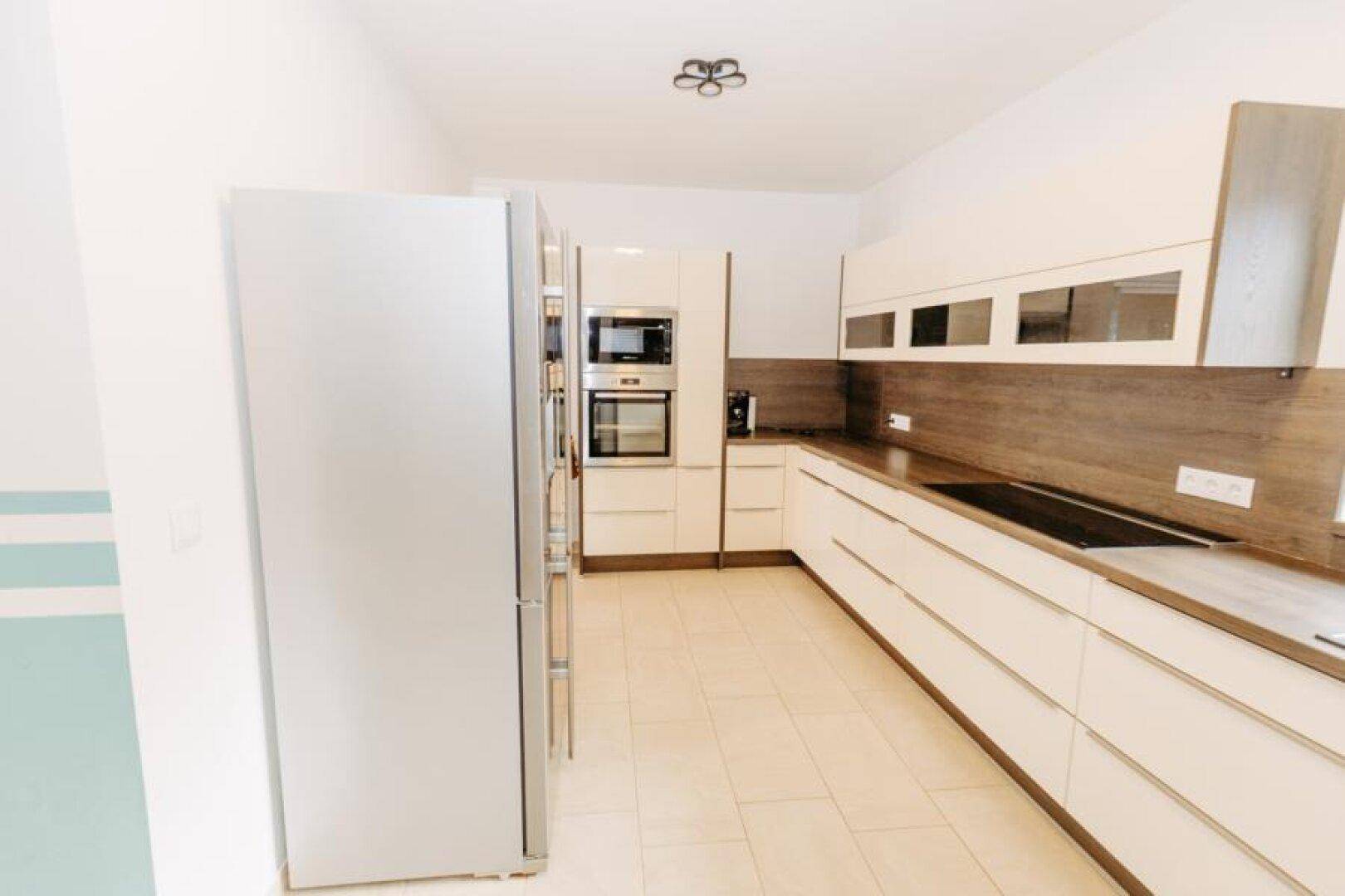 Stilvolle Küche mit weißen Hochglanzfronten, Holzdetails und modernen Einbaugeräten.