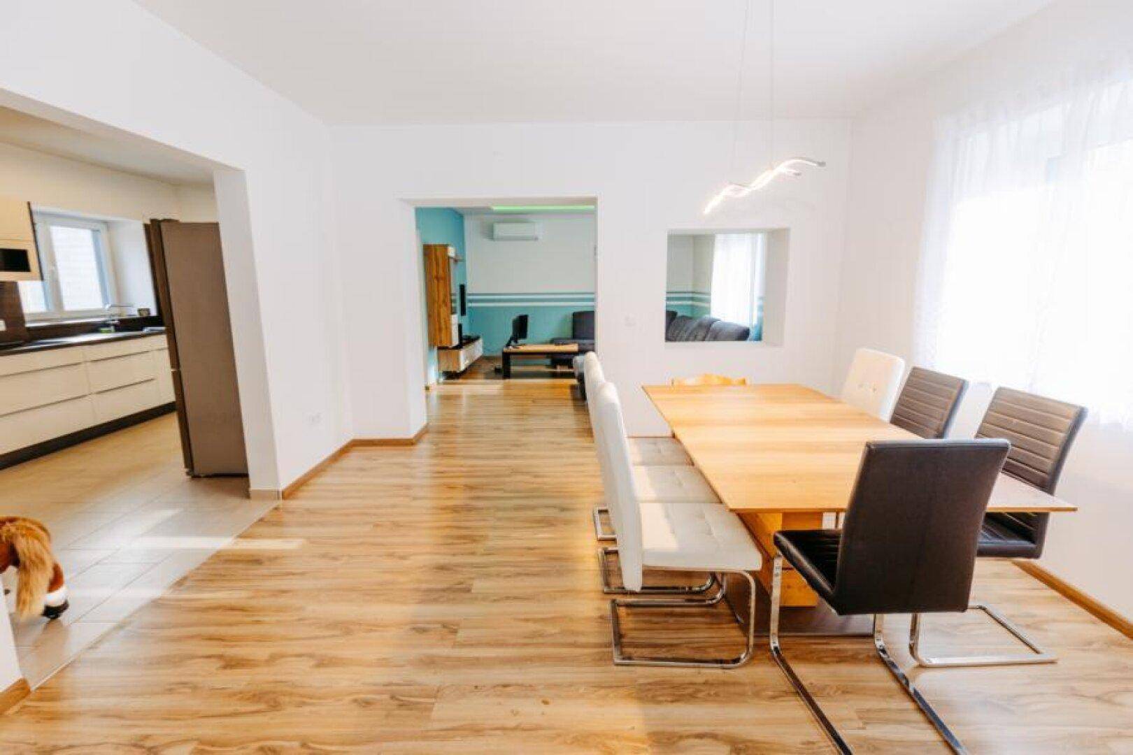 Heller Essbereich mit großem Holztisch, modernen Stühlen und Blick in Küche und Wohnzimmer.