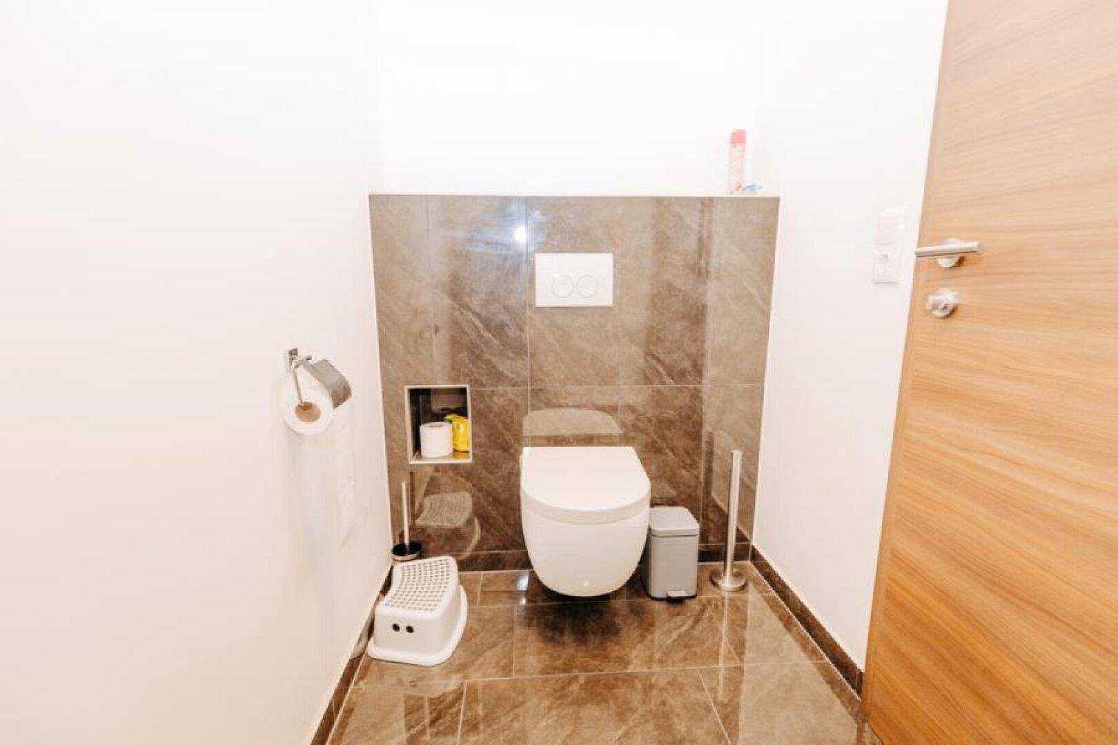 Modernes Gäste-WC mit Wand-WC, dunklen Fliesen und minimalistischem Design.