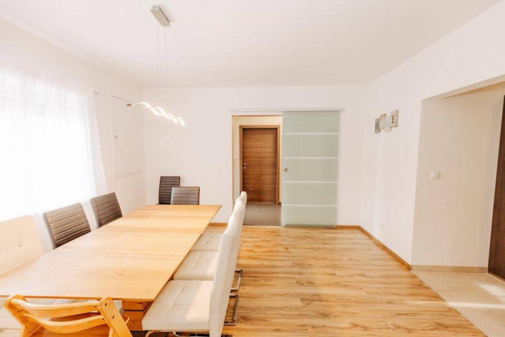 Essbereich mit Holzboden und einer modernen Glasschiebetür, die zu einem weiteren Raum führt.