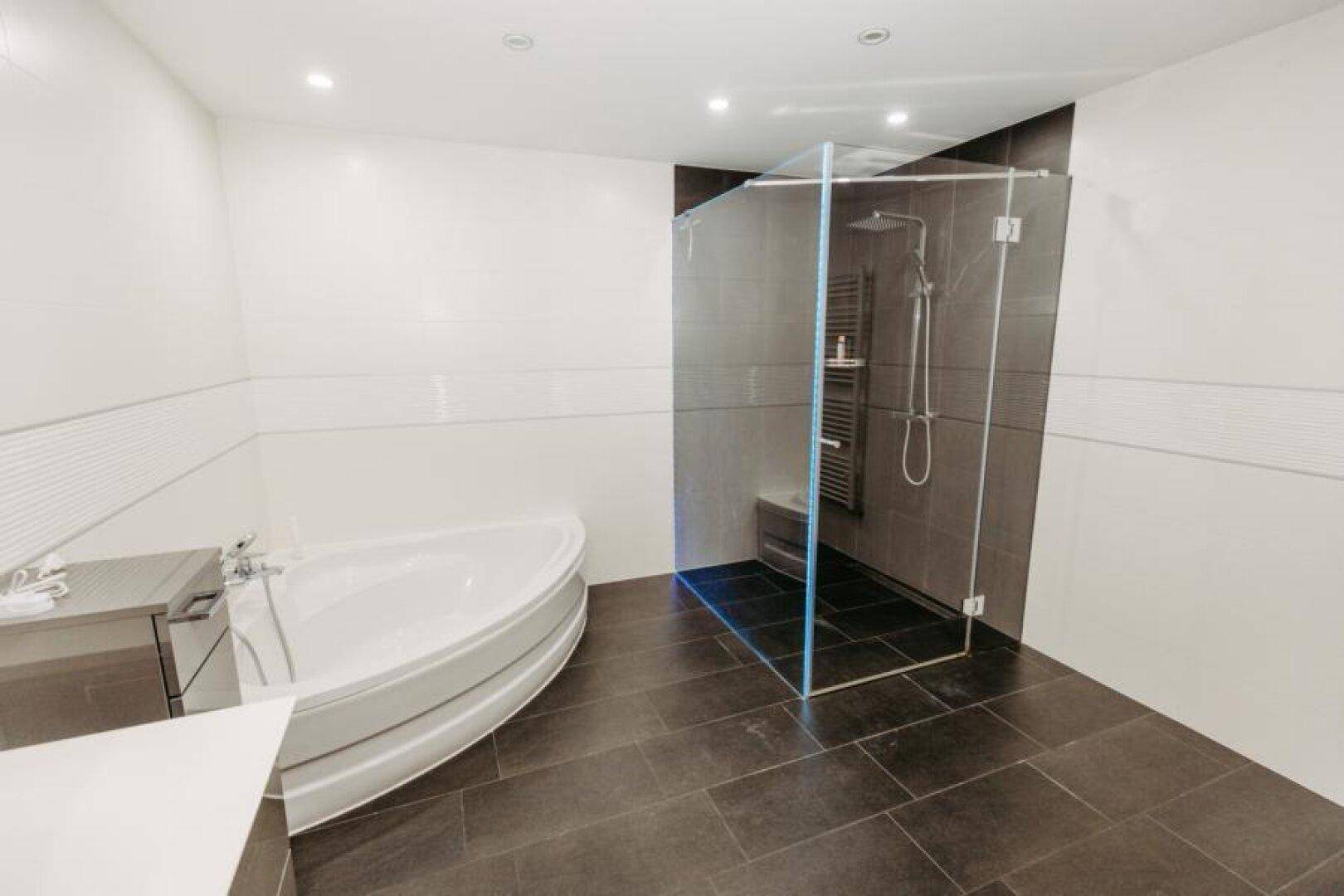 Geräumiges Badezimmer mit moderner Duschkabine, Eckbadewanne und dunklem Fliesenboden.