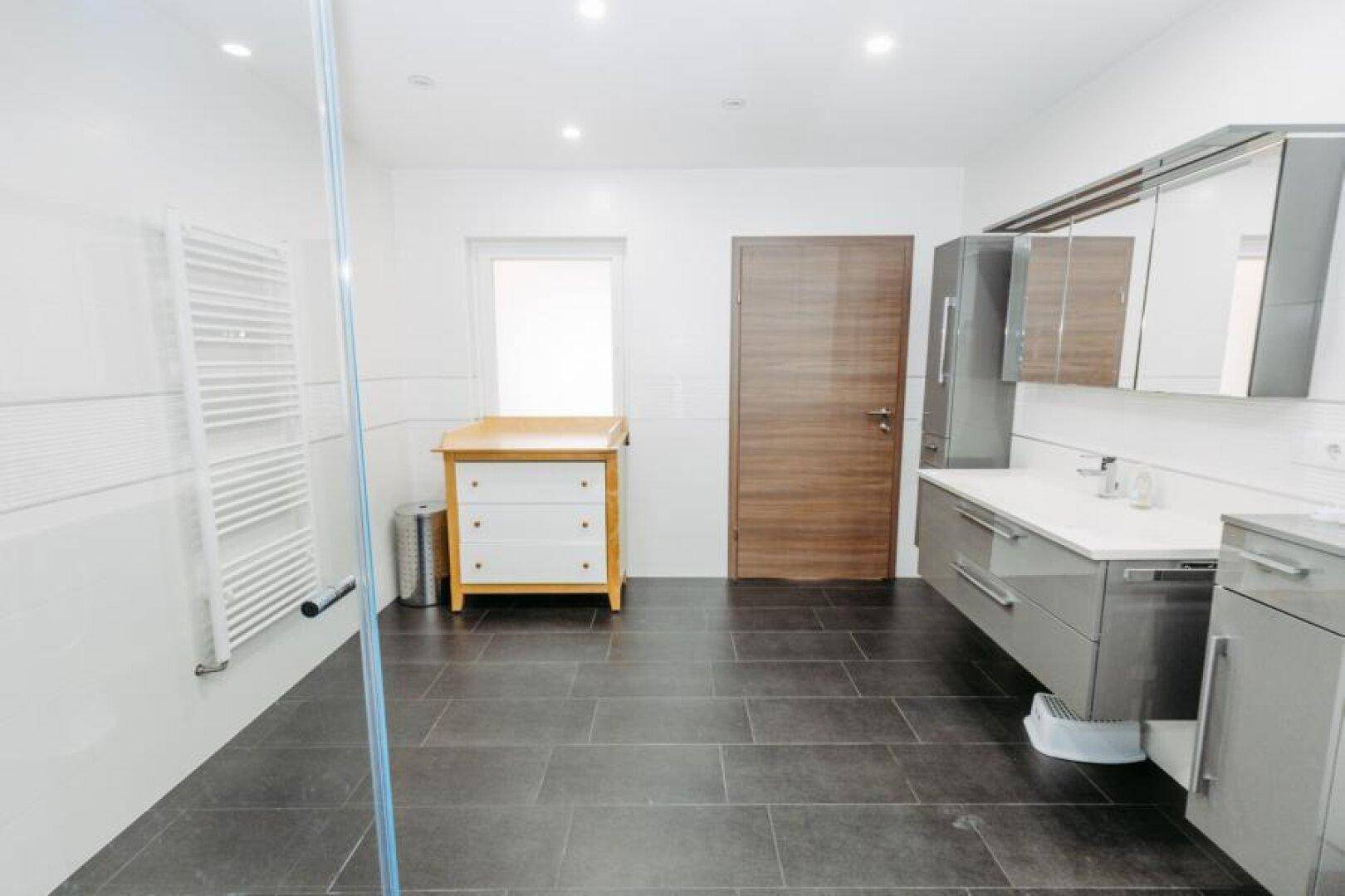 Helles Badezimmer mit Fenster, Wickeltisch und modernen Badmöbeln in Grau.
