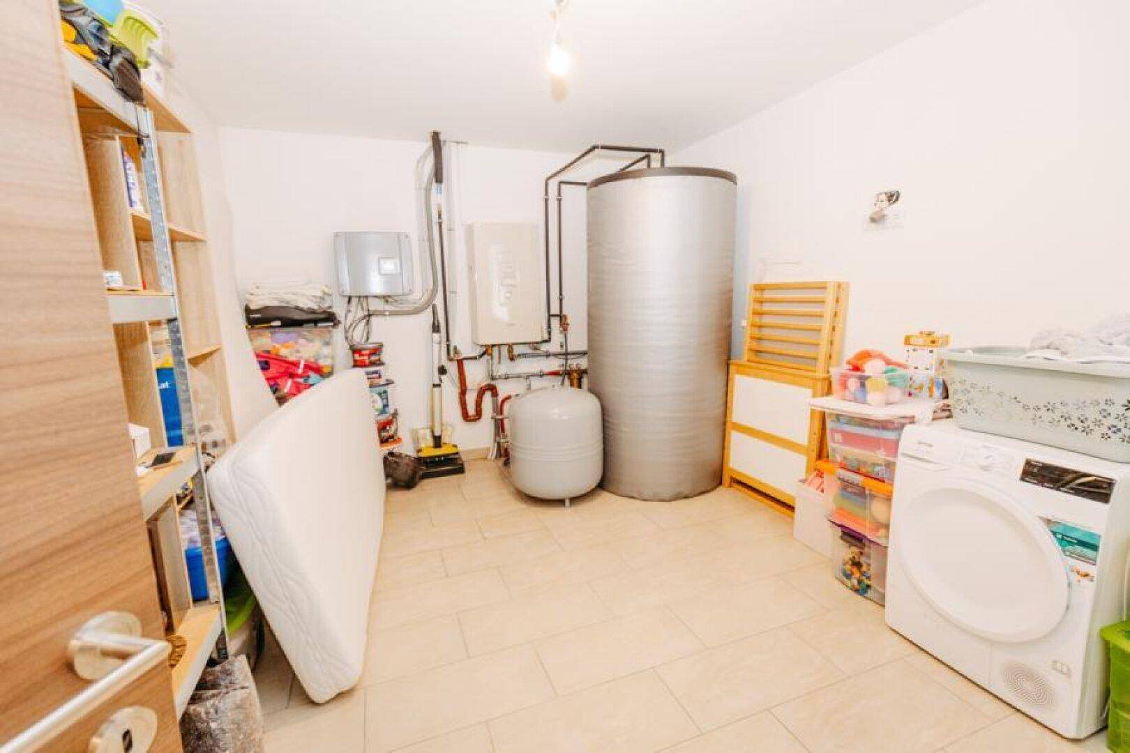 Hauswirtschaftsraum mit Waschmaschine, Warmwasserspeicher und Regalen für Lagerung.
