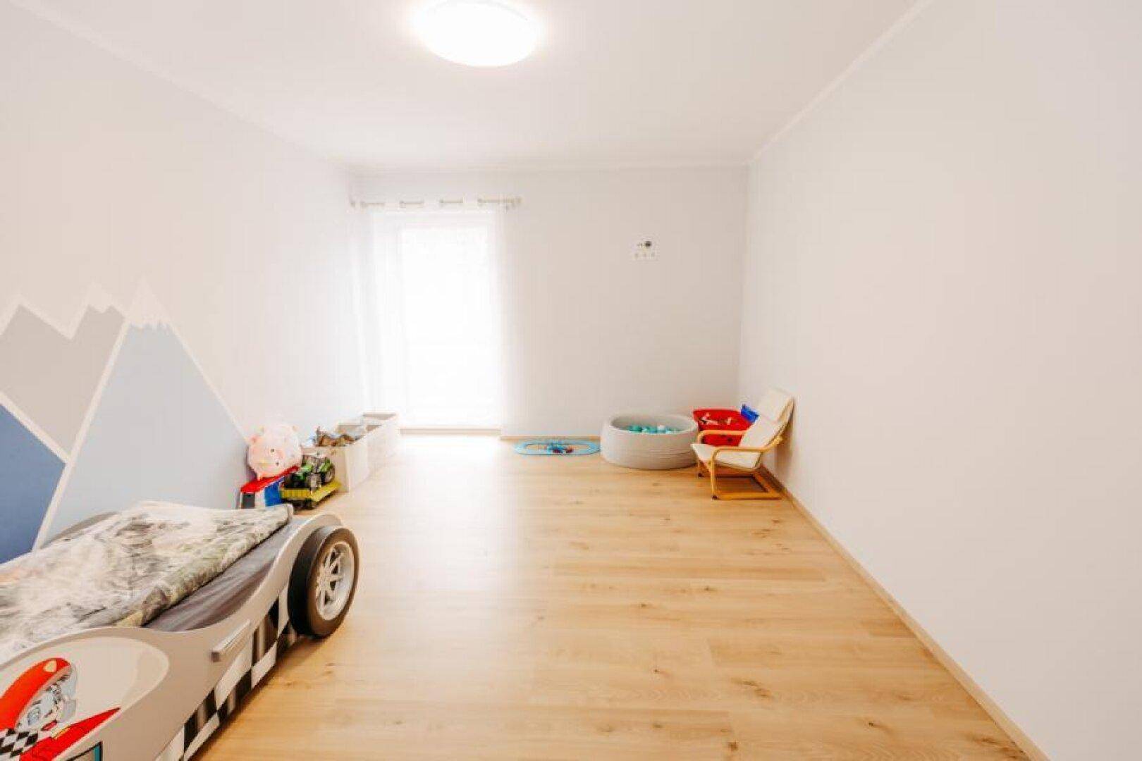Kinderzimmer mit Rennwagenbett, hellem Holzboden und Bergmotiv-Wandmalerei.