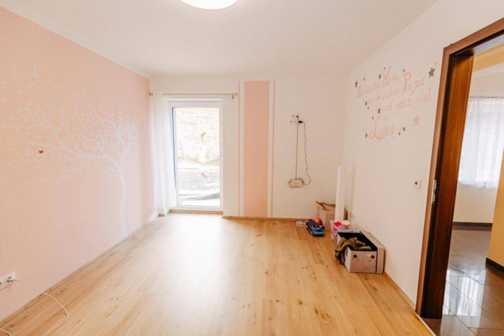 Helles Kinderzimmer mit Holzboden, rosa Wänden und Zugang zum Außenbereich.