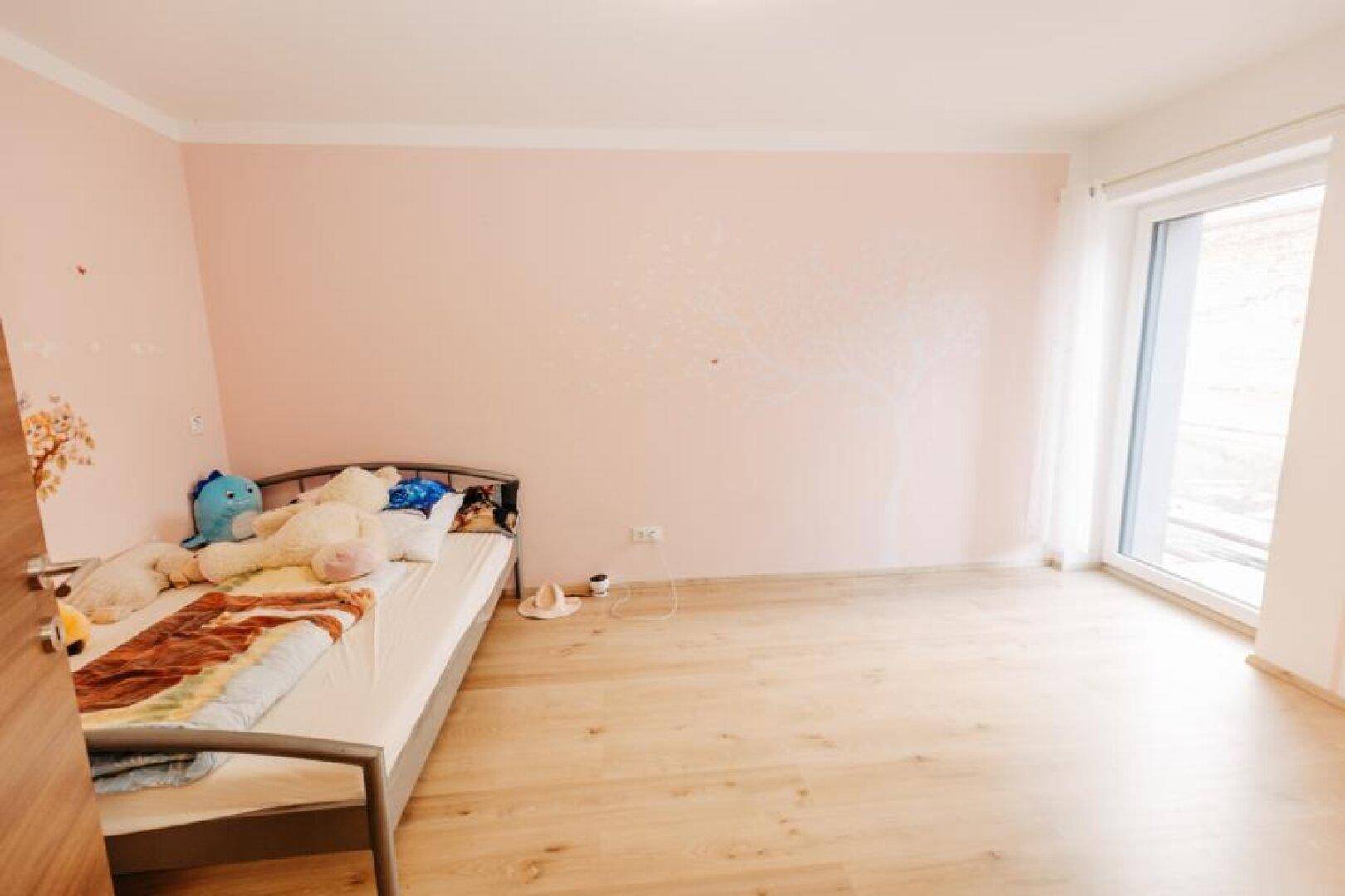 Kinderzimmer mit Einzelbett, hellem Holzboden und rosa Wänden mit Wanddekoration.