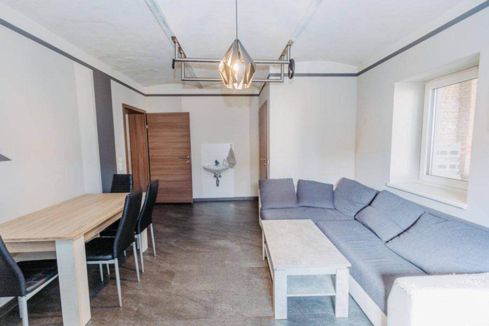 Rustikaler Wohn-Essbereich mit Holztisch, Sofa und freiliegenden Deckenbalken.