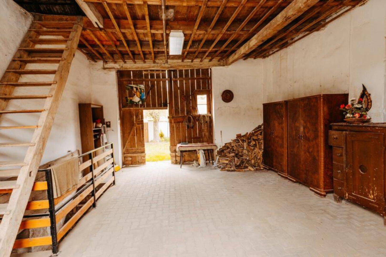Geräumiger Abstellraum mit Holzbalken, Ziegelboden und gestapeltem Brennholz.