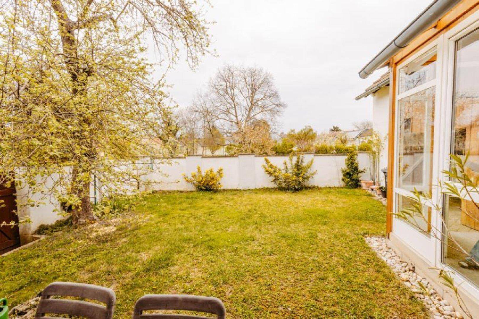 Weitläufiger Garten mit Rasen, Bäumen und einer kleinen Terrasse am Haus.