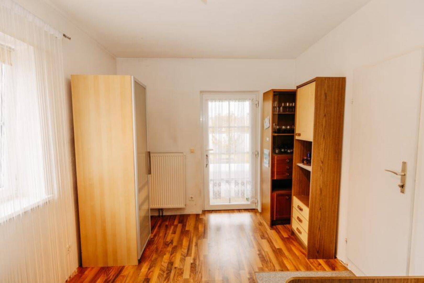 Schlafzimmer mit Holzboden, Kleiderschrank und Zugang zu einem weiteren Raum.