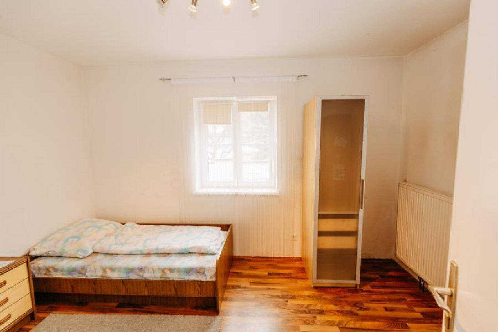 Gemütliches Schlafzimmer mit Einzelbett, Holzboden und Fenster für natürliches Licht.