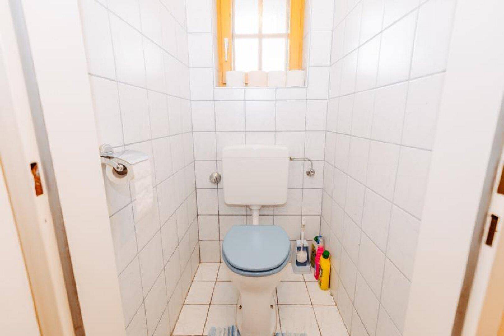 Kleines Gäste-WC mit weißen Fliesen und Fenster für natürliche Belüftung.