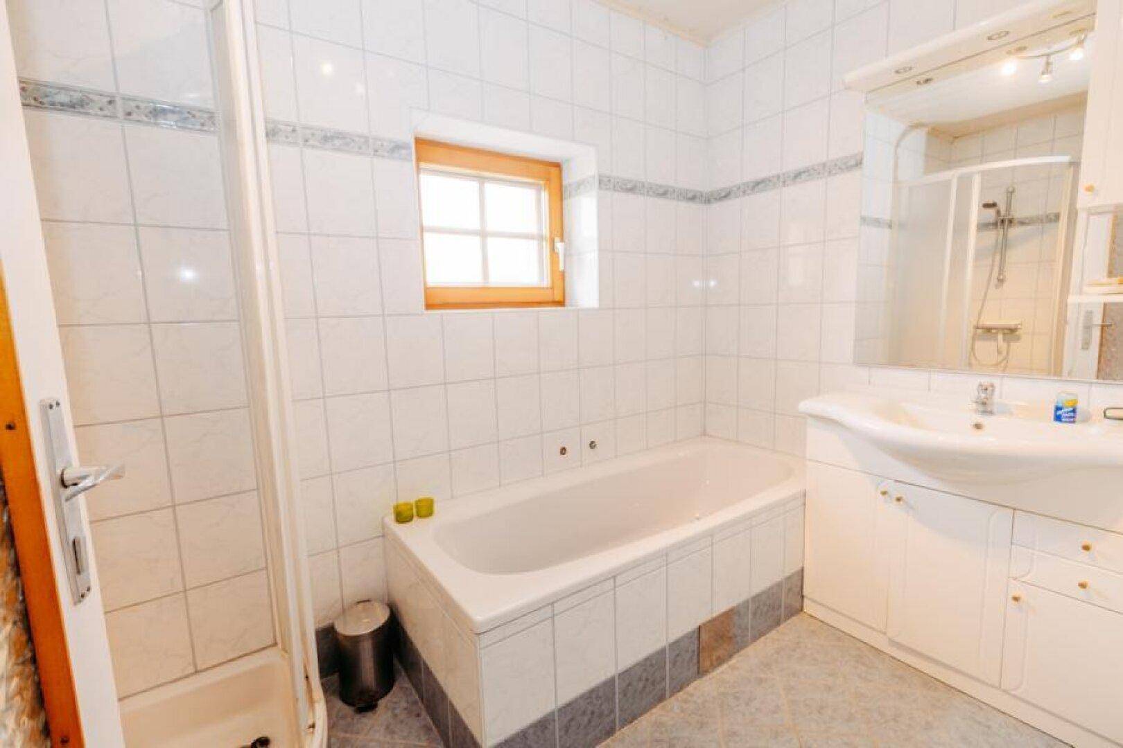 Gefliestes Badezimmer mit Badewanne, Duschkabine und Waschbecken mit Unterschrank.