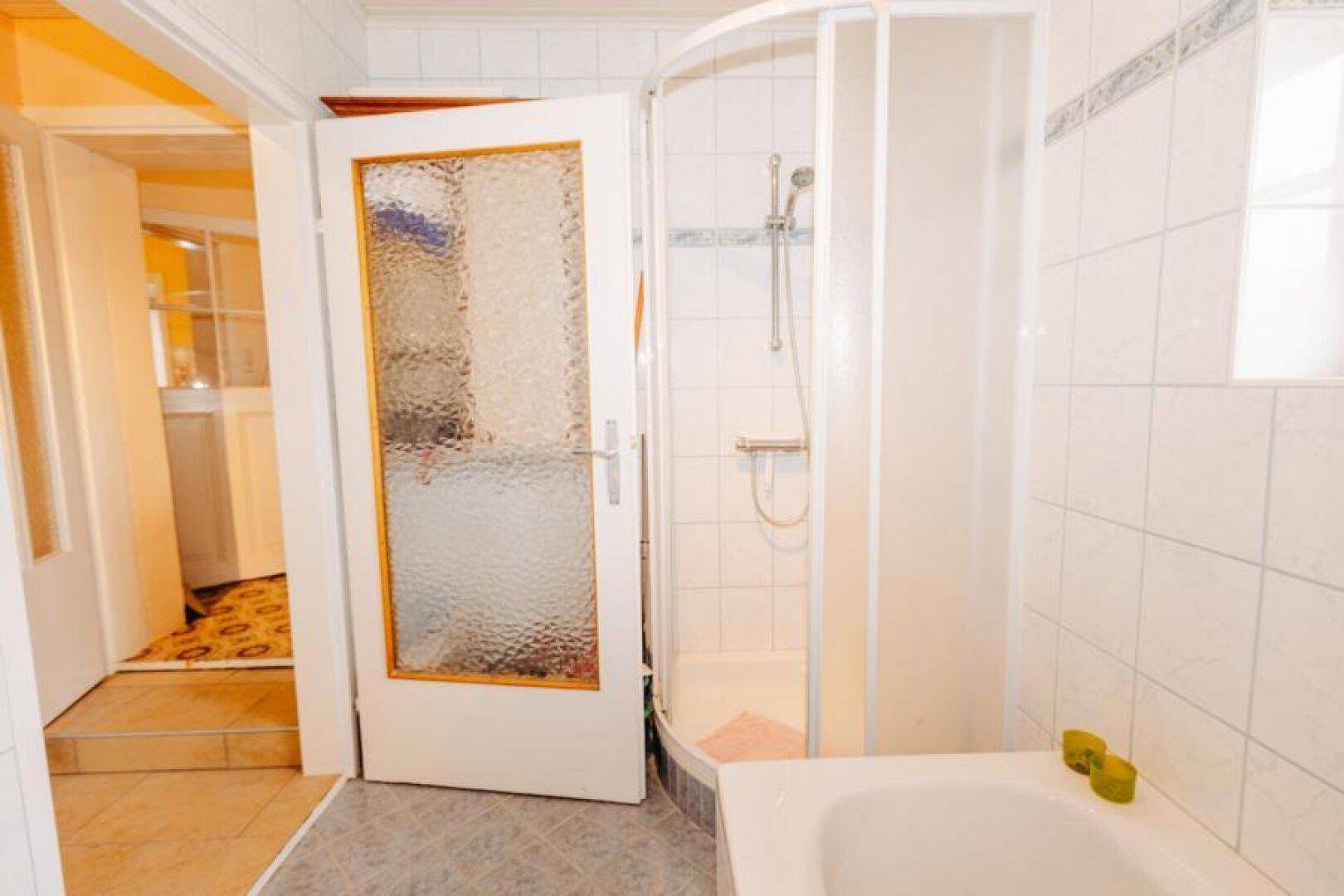 Badezimmer mit Duschkabine, weißen Fliesen und Zugang zum Flur.