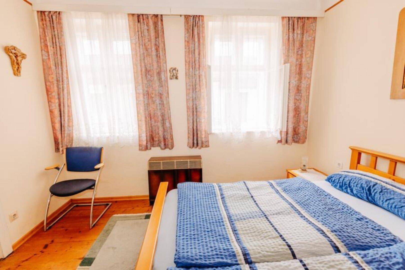 Helles Schlafzimmer mit Doppelbett, Fenster und Holzboden für eine warme Atmosphäre.