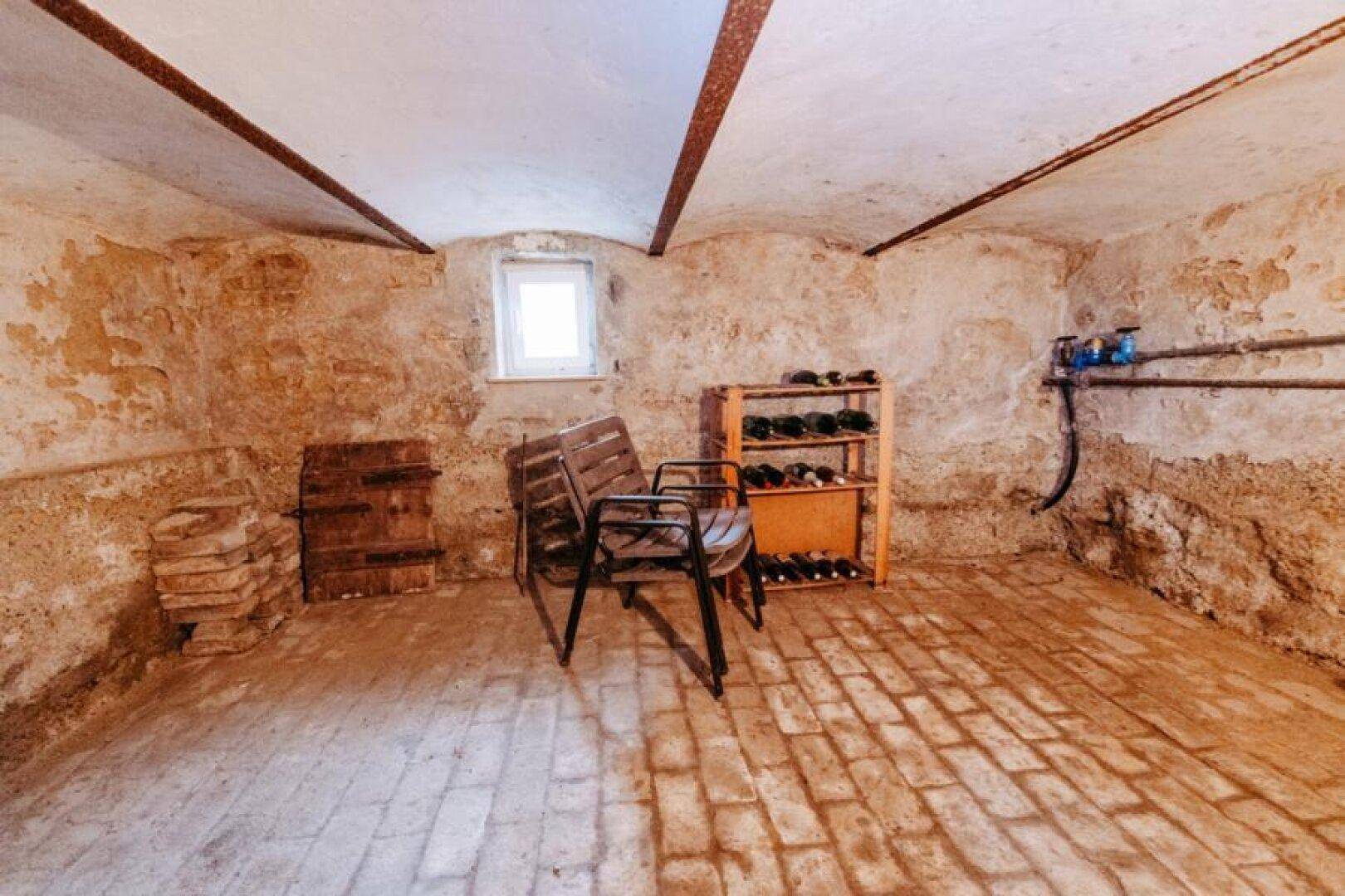 Kellerraum mit unverputzten Wänden, Ziegelboden und Weinlagerung.