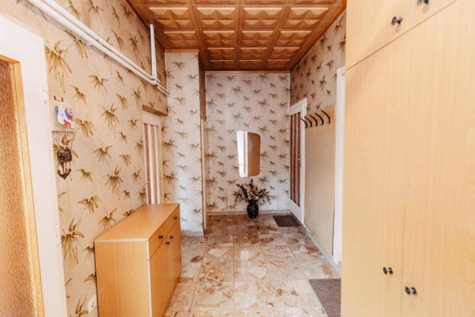 Flur mit gemusterten Tapeten, Fliesenboden und Holzschränken im Vintage-Stil.