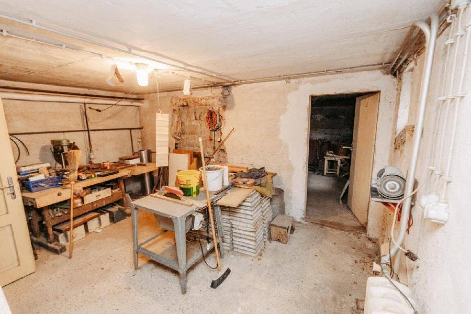 Werkstatt im Keller mit Werkbänken, Werkzeugen und verschiedenen Materialien.