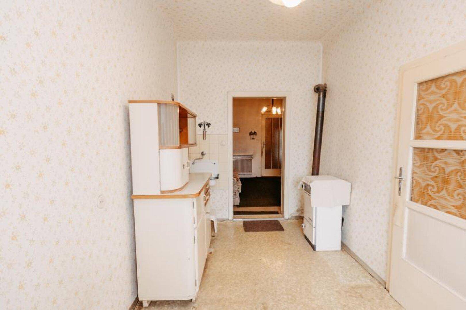 Einfache Küche mit älteren Küchenmöbeln, Spüle und einem Ofen im Landhausstil.