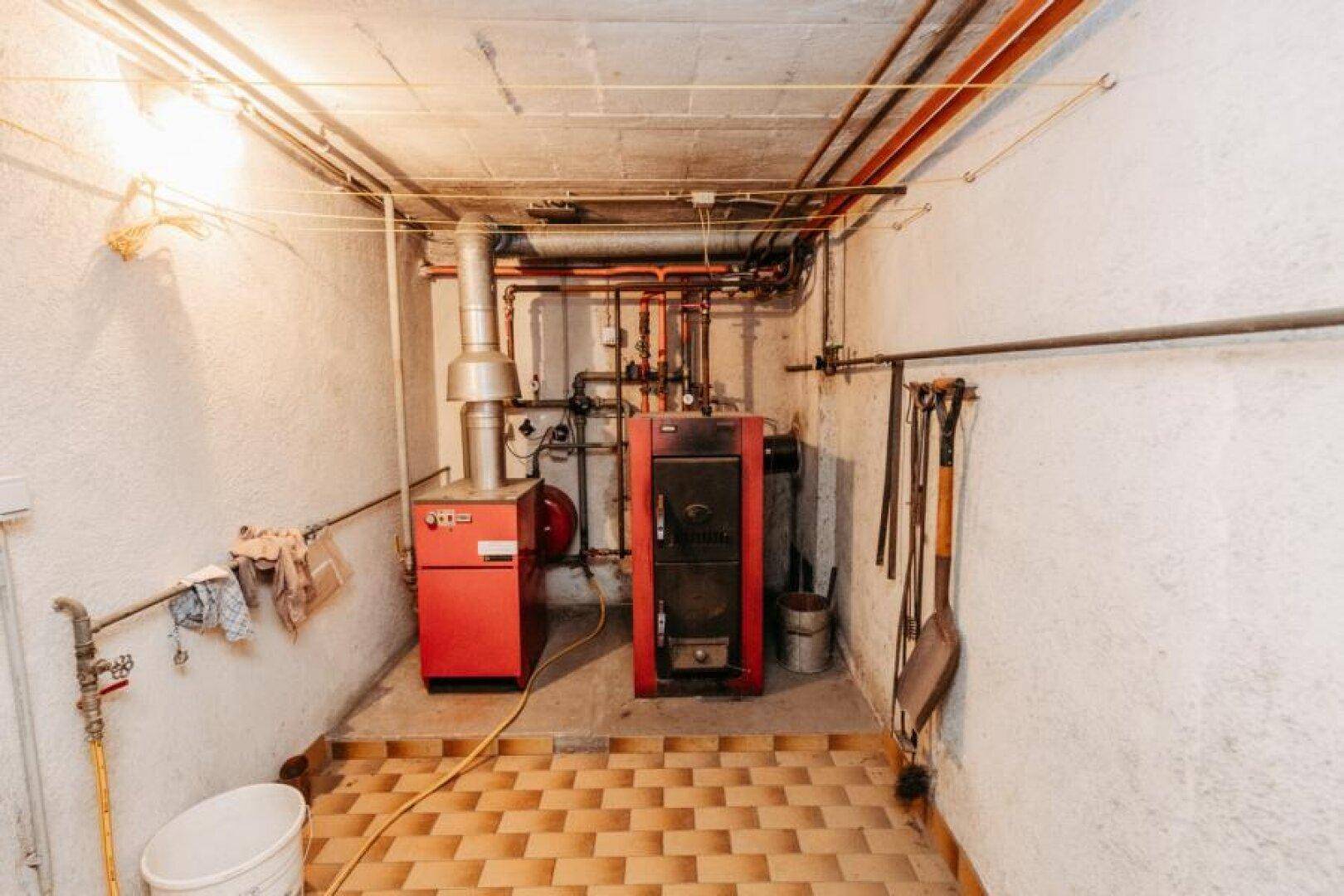 Heizungsraum im Keller mit zwei Heizkesseln und sichtbaren Rohrleitungen.