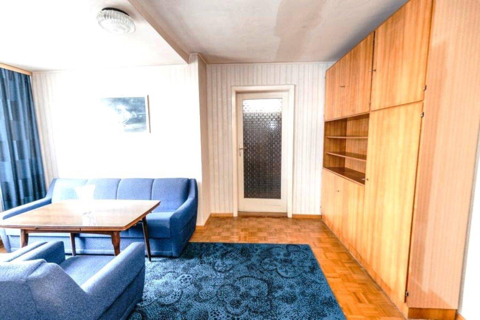 Wohnraum mit blauen Sofas, Teppichboden und Holzschränken.