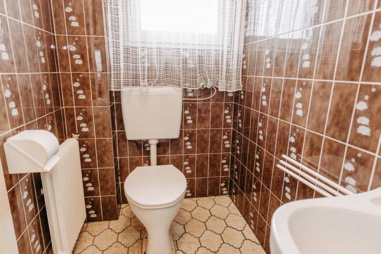 Badezimmer mit braunen Fliesen, Toilette und kleinem Waschbecken.