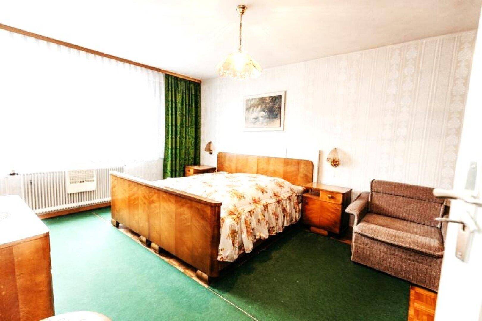 Schlafzimmer mit Holzdoppelbett, grünem Teppichboden und traditioneller Einrichtung.