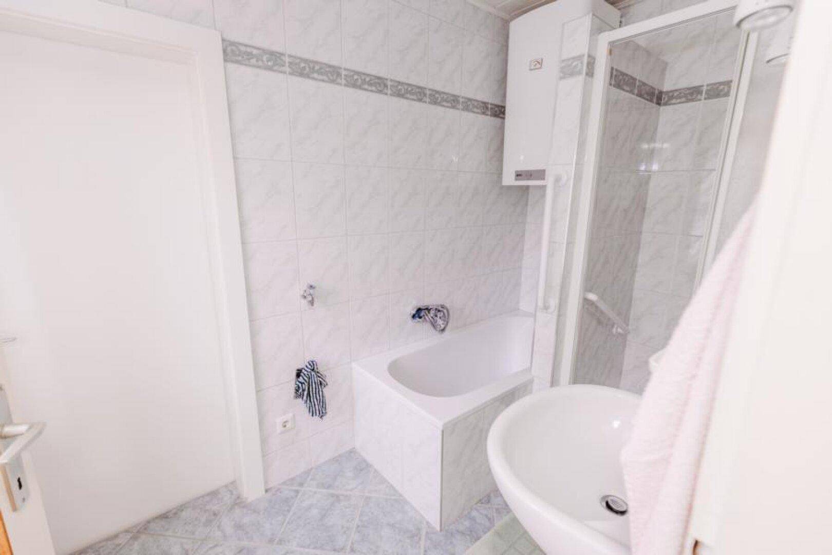 Badezimmer mit Badewanne, Duschkabine, Waschbecken und hellen Fliesen.