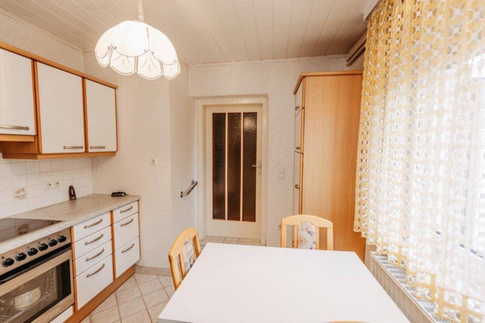 Einbauküche mit Essbereich, weißen Schränken und Fenster mit Vorhängen.