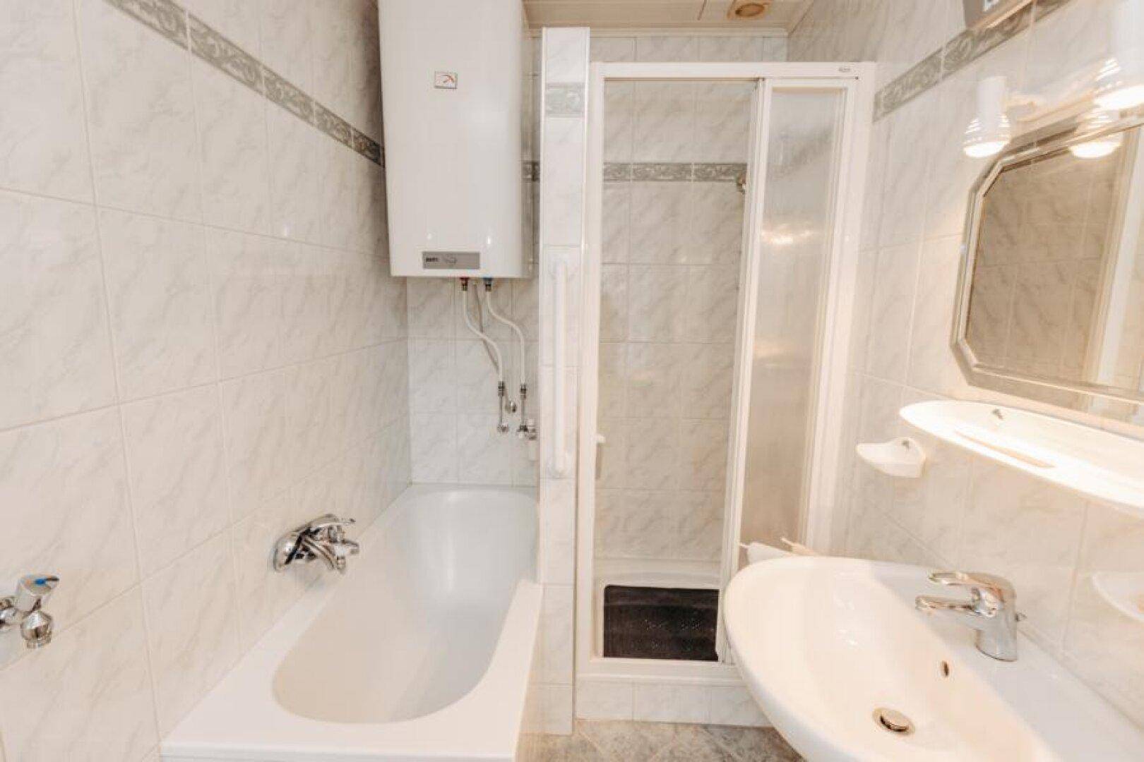 Helles Badezimmer mit Badewanne, Duschkabine, Waschbecken und Spiegel.