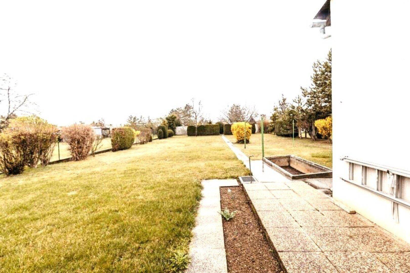 Weitläufiger Gartenbereich mit Rasen, Sträuchern und einem gepflasterten Weg entlang des Hauses.