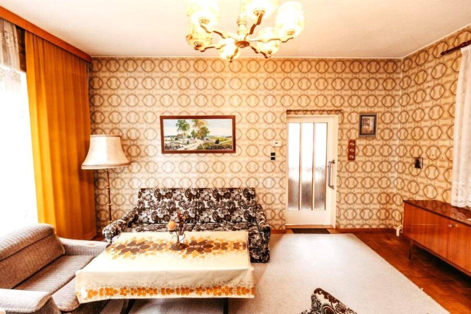 Wohnzimmer im Vintage-Stil mit gemusterter Tapete, Teppichboden und traditionellen Möbeln.