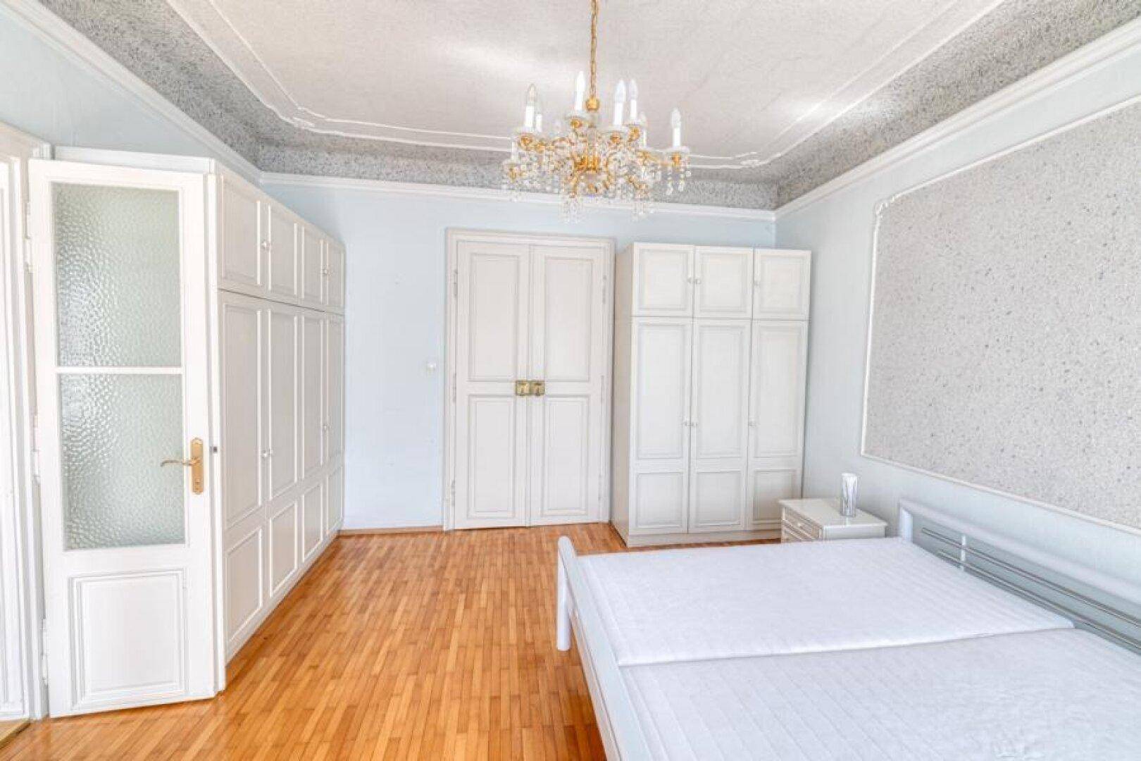 Geräumiges Schlafzimmer mit Parkettboden, weißen Einbauschränken und Kronleuchter.