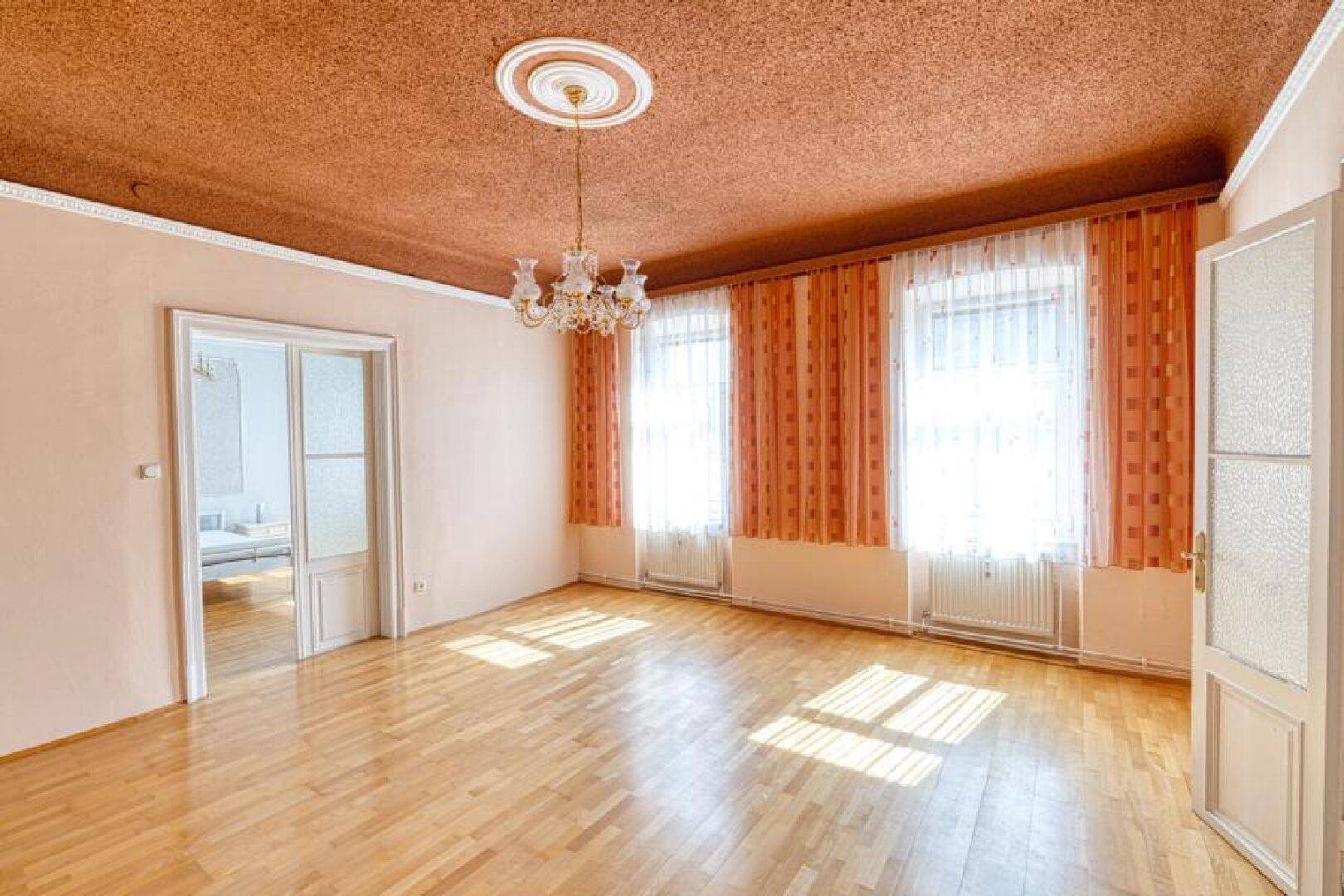 Helles Wohnzimmer mit Parkettboden, hohen Decken und Kronleuchter.