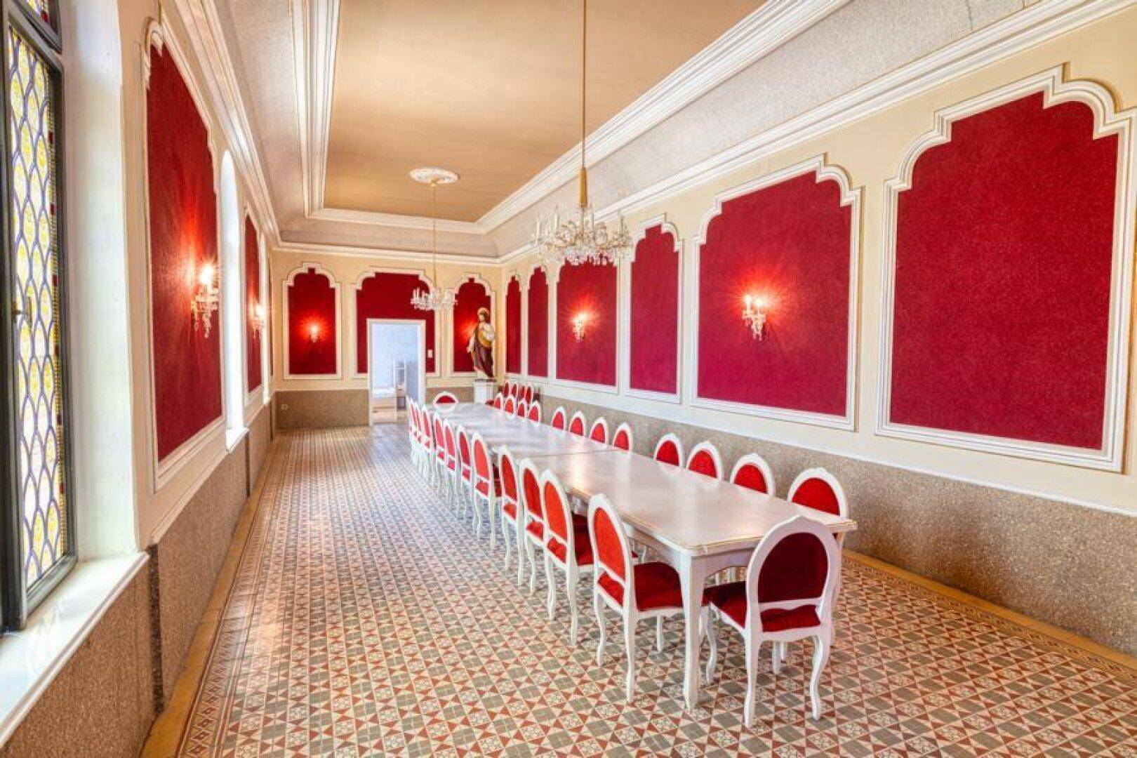 Großer, prunkvoller Speisesaal mit langen Tischen, roten Stühlen und verzierten Wänden.