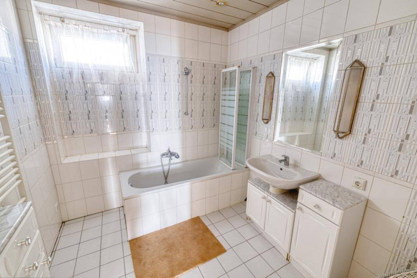 Gefliestes Badezimmer mit Badewanne, Dusche, Waschbecken und Fenster.