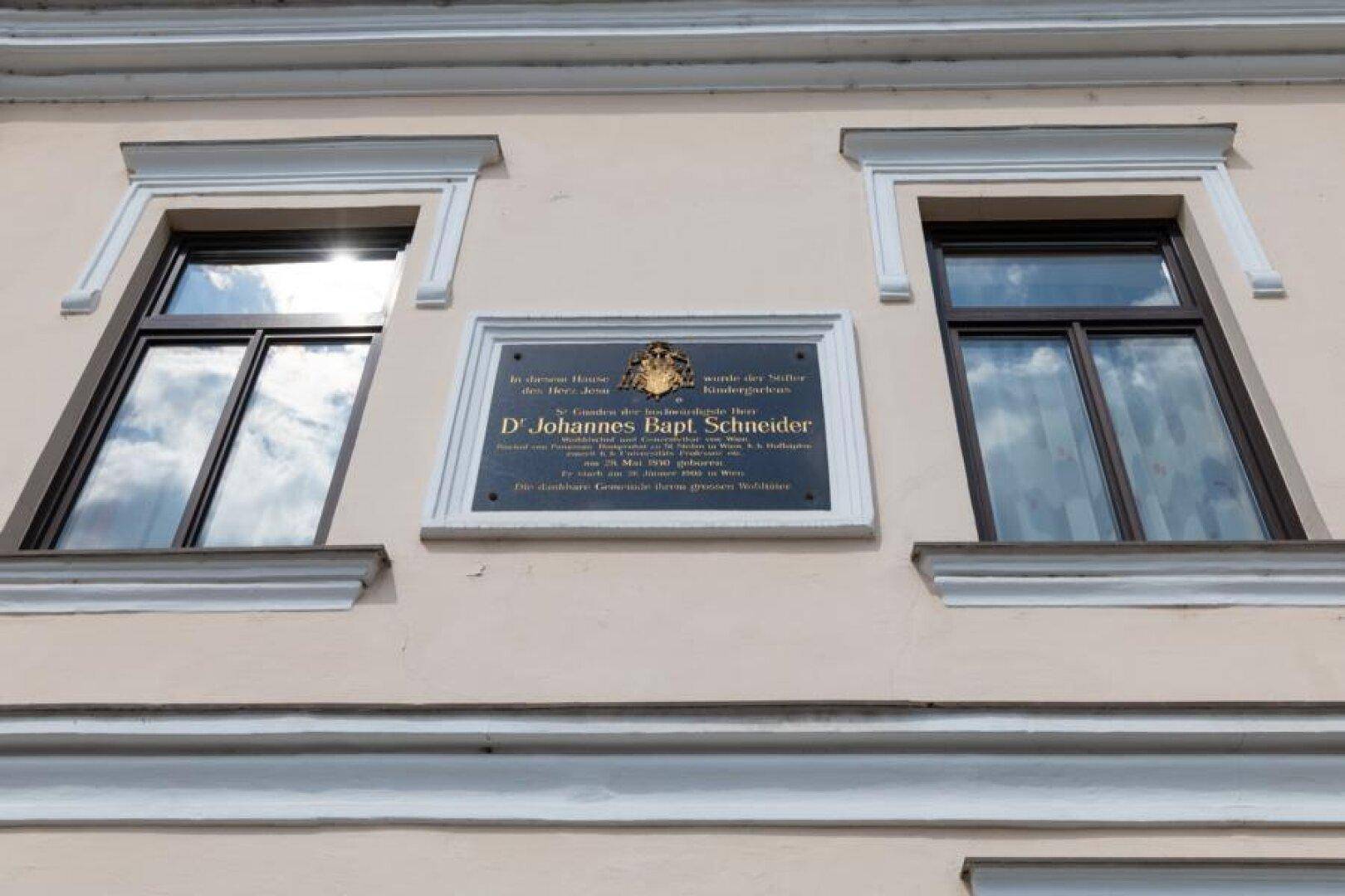 Detailansicht der historischen Fassade mit Gedenktafel und verzierten Fenstern.