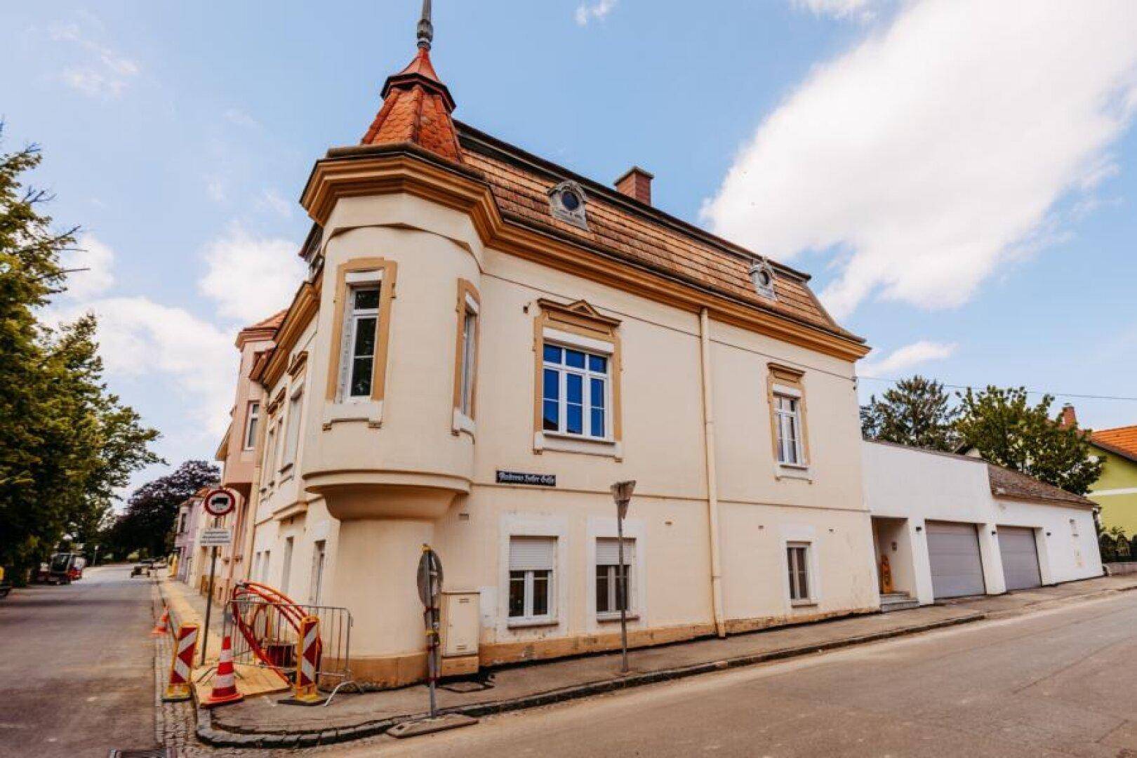 Ansicht des historischen Eckgebäudes mit Garagen und Mansarddach an einer ruhigen Straße.