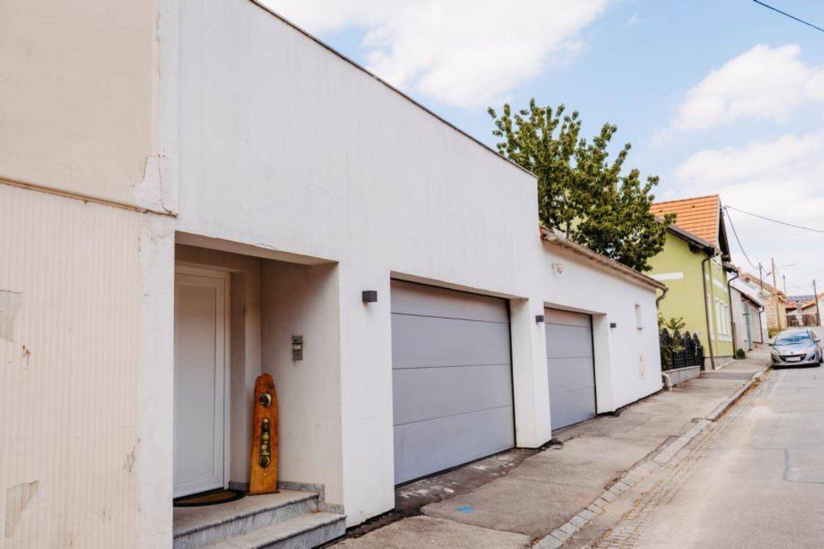 Moderne weiße Fassade mit zwei Garagentoren und einem Eingangsbereich an der Straße.