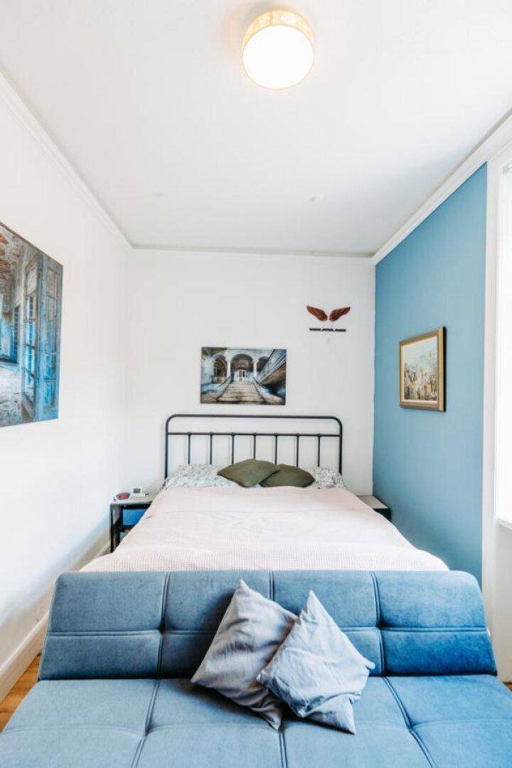 Gemütliches Schlafzimmer mit blauem Akzentwand, Doppelbett und Sofa.